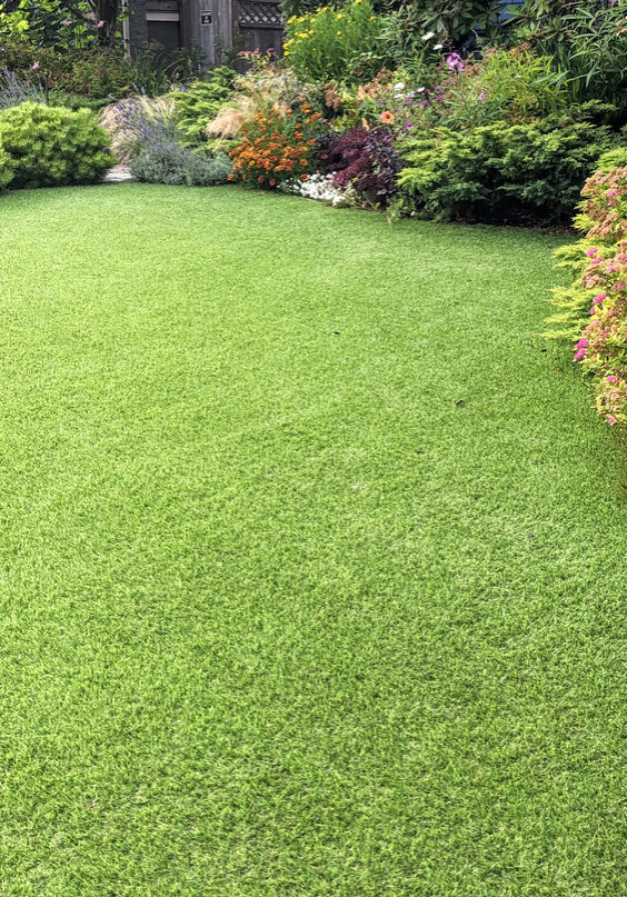 A beautiful artificial lawn in the front yard with nice flowers and shrubs surrounding it